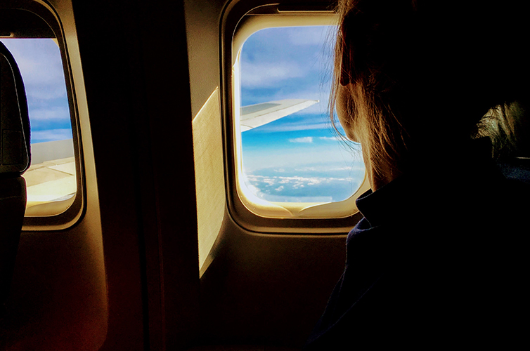 Young woman looking out of plane window to blue sky and clouds